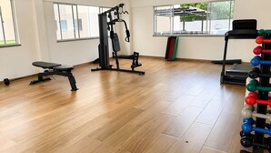 Un gimnasio con equipo de ejercicio, una banca, una cinta de correr y ventanas con vistas.