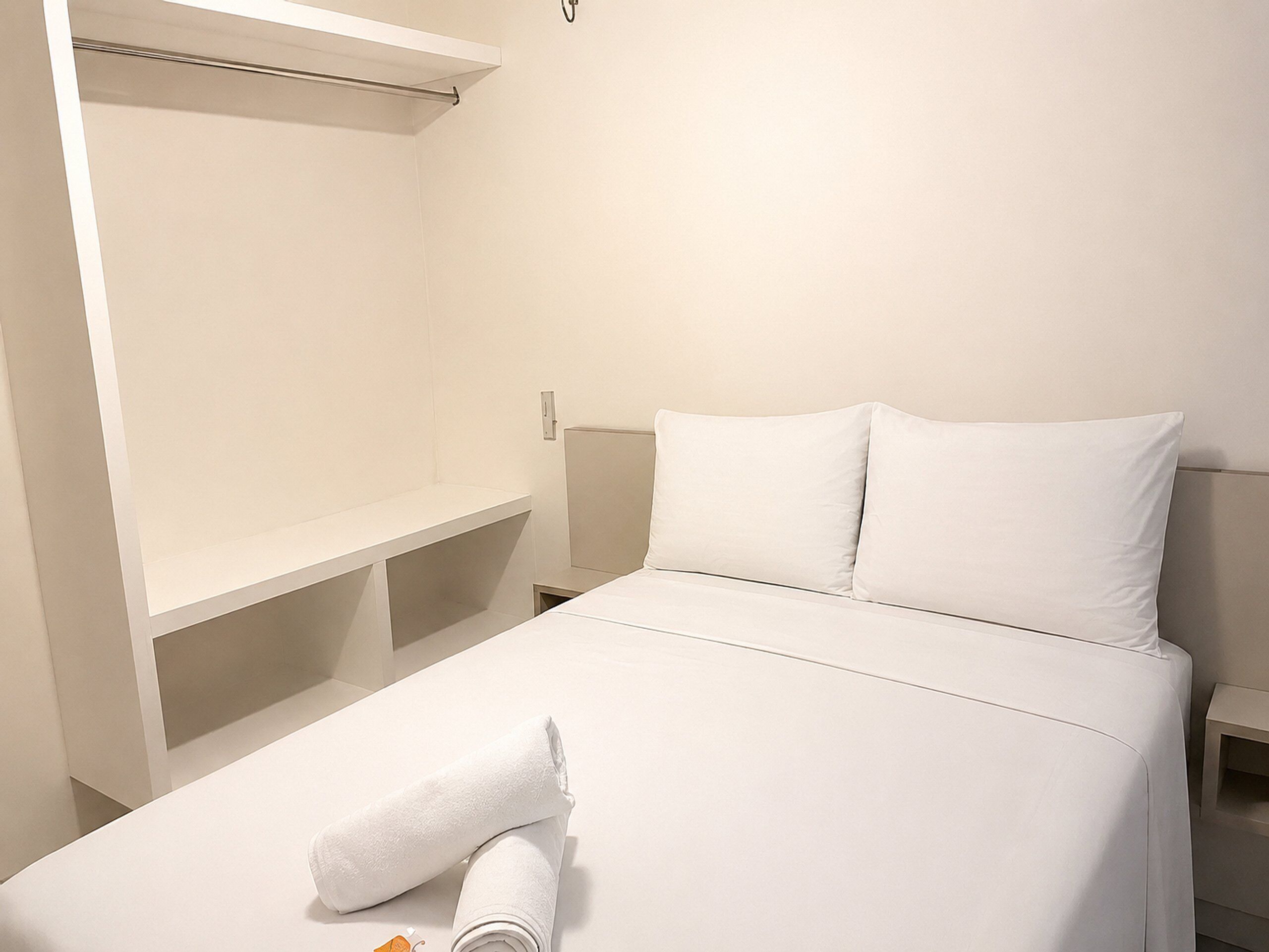 A hotel room with a bed, a nightstand, a wardrobe, and a towel on the bed.