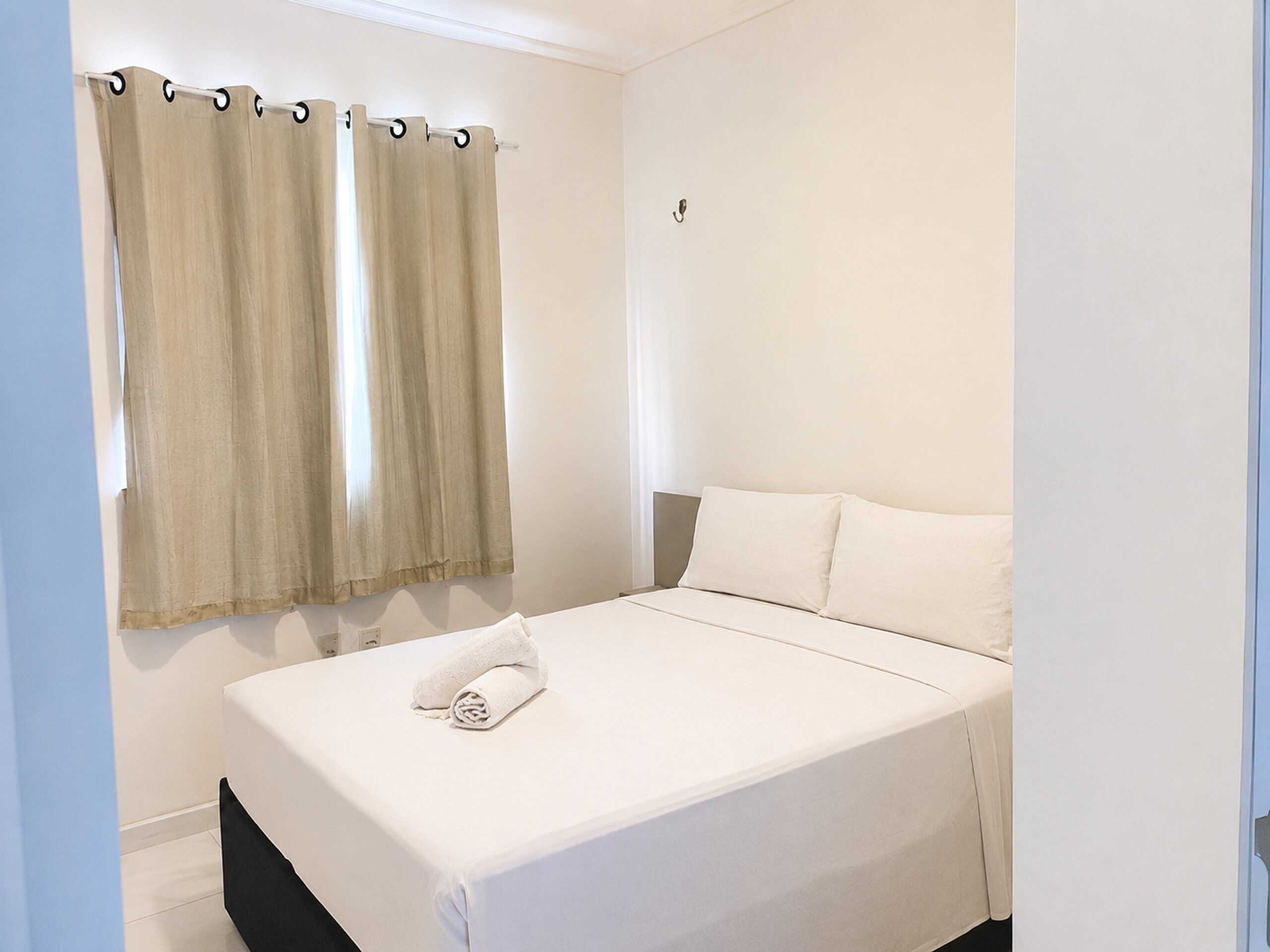 A bedroom with a bed, curtains, and a wall-mounted hook.