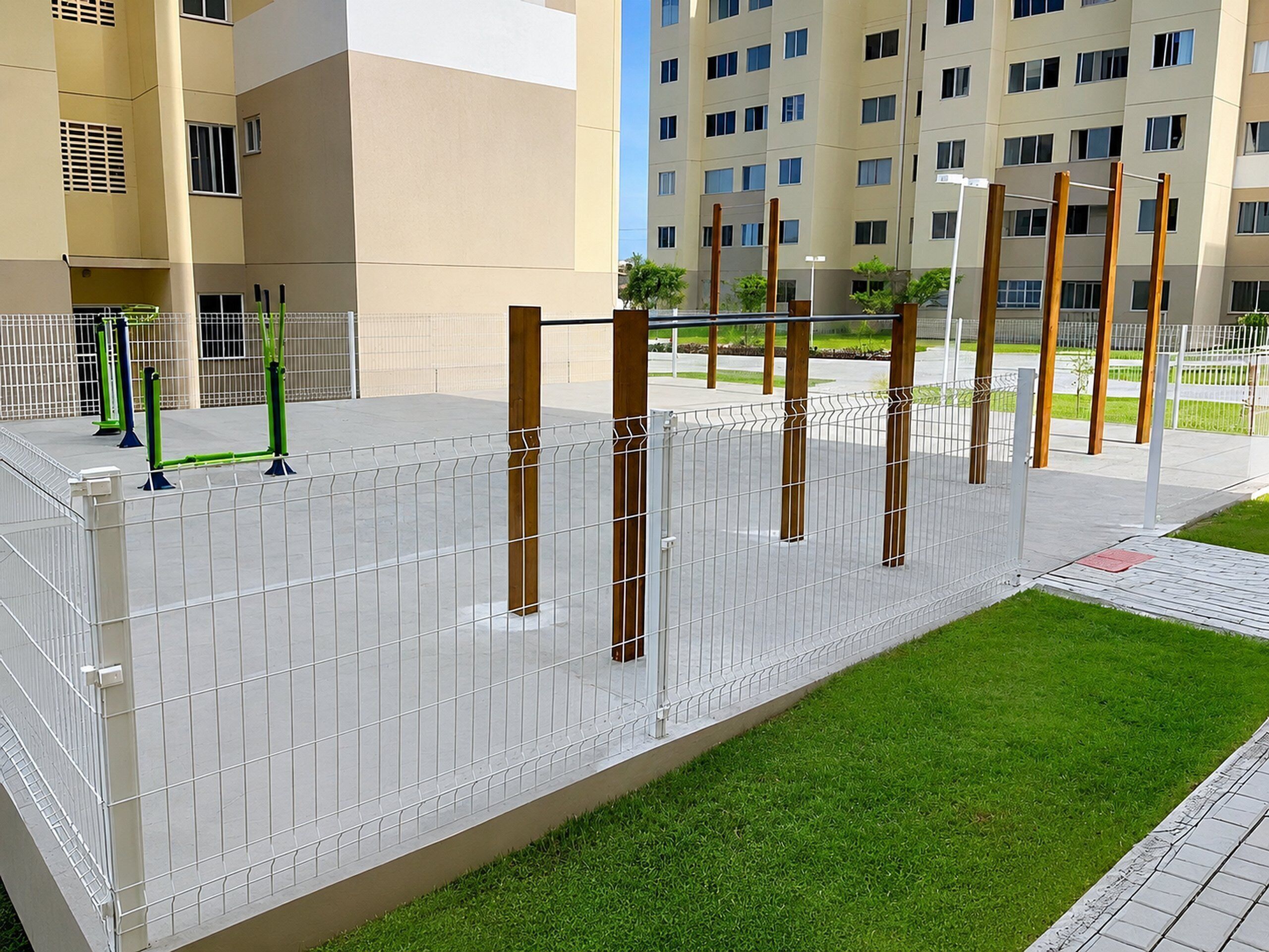 A fenced outdoor area with exercise equipment, a grassy patch, and a building in the background.