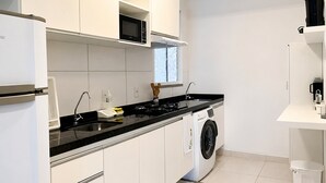 Una cocina moderna con armarios blancos, encimera negra, microondas, lavadora y cafetera.