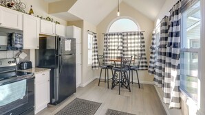 A kitchen with a black refrigerator, white cabinets, a dining table with chairs, and a window with checkered curtains. - Wichita Townhome w/ Patio: 9 Mi to Downtown! (Wichita)