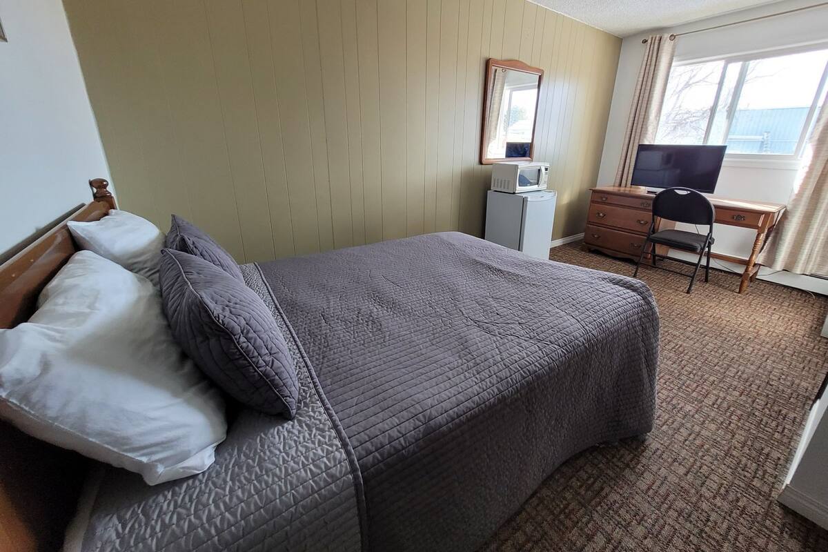 A hotel room with a bed, a dresser, a desk, a chair, a television, and a window.