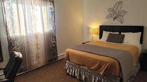 A hotel room with a bed, a chair, a lamp, and a wall art piece.