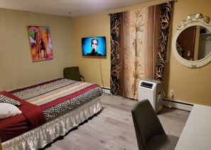Ein Hotelzimmer mit Bett, Sessel, Fernseher, Vorhängen, Spiegel und Klimaanlage.
