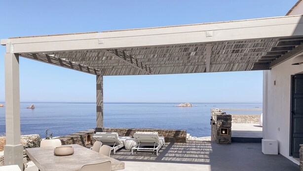 An outdoor patio with a table and chairs, a pergola, and a view of the sea. - Cliff Villa  (Paros)