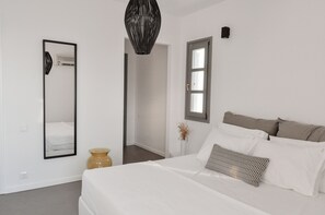 Une chambre à coucher moderne avec un grand lit, un miroir, une fenêtre et un vase contenant des plantes séchées.
