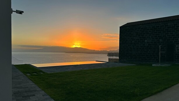 A sunset view from a building with a brick wall and a grassy area in front. - Casa da Arribana (Ponta Delgada)