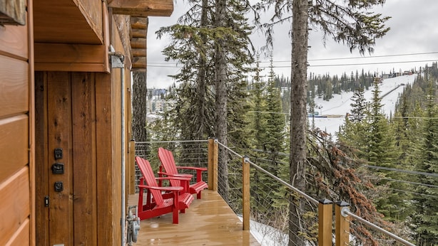 Una terraza de madera con sillas rojas que da a un paisaje nevado y un bosque denso.