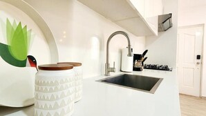 A modern kitchen with a white countertop, a stainless steel sink, and a white cabinet with a decorative pineapple design. - Apartamento Bayahibe Con Terraza (San Rafael del Yuma)