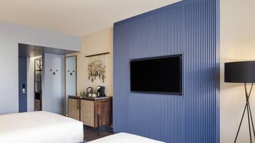 A hotel room with a large TV mounted on a blue wall, a wooden dresser, a bed, and a mirror.