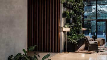 Un hall d’entrée moderne doté d’une grande fenêtre, d’un mur végétal vertical et d’un espace détente avec un lampadaire.