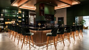 Una zona de bar con una barra de madera curvada, varios taburetes y estantes con botellas y objetos decorativos.