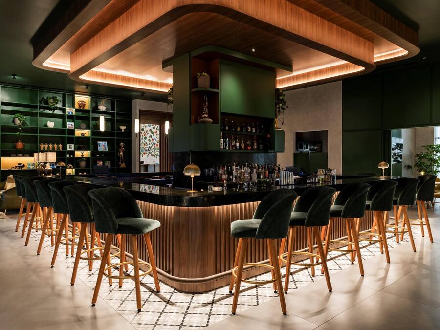 Un espace bar doté d’un comptoir en bois incurvé, de plusieurs tabourets de bar et d’étagères où sont exposées des bouteilles et des objets décoratifs.