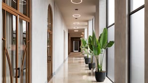 Un pasillo moderno de hotel con puertas de cristal, plantas en macetas y un suelo limpio y pulido.