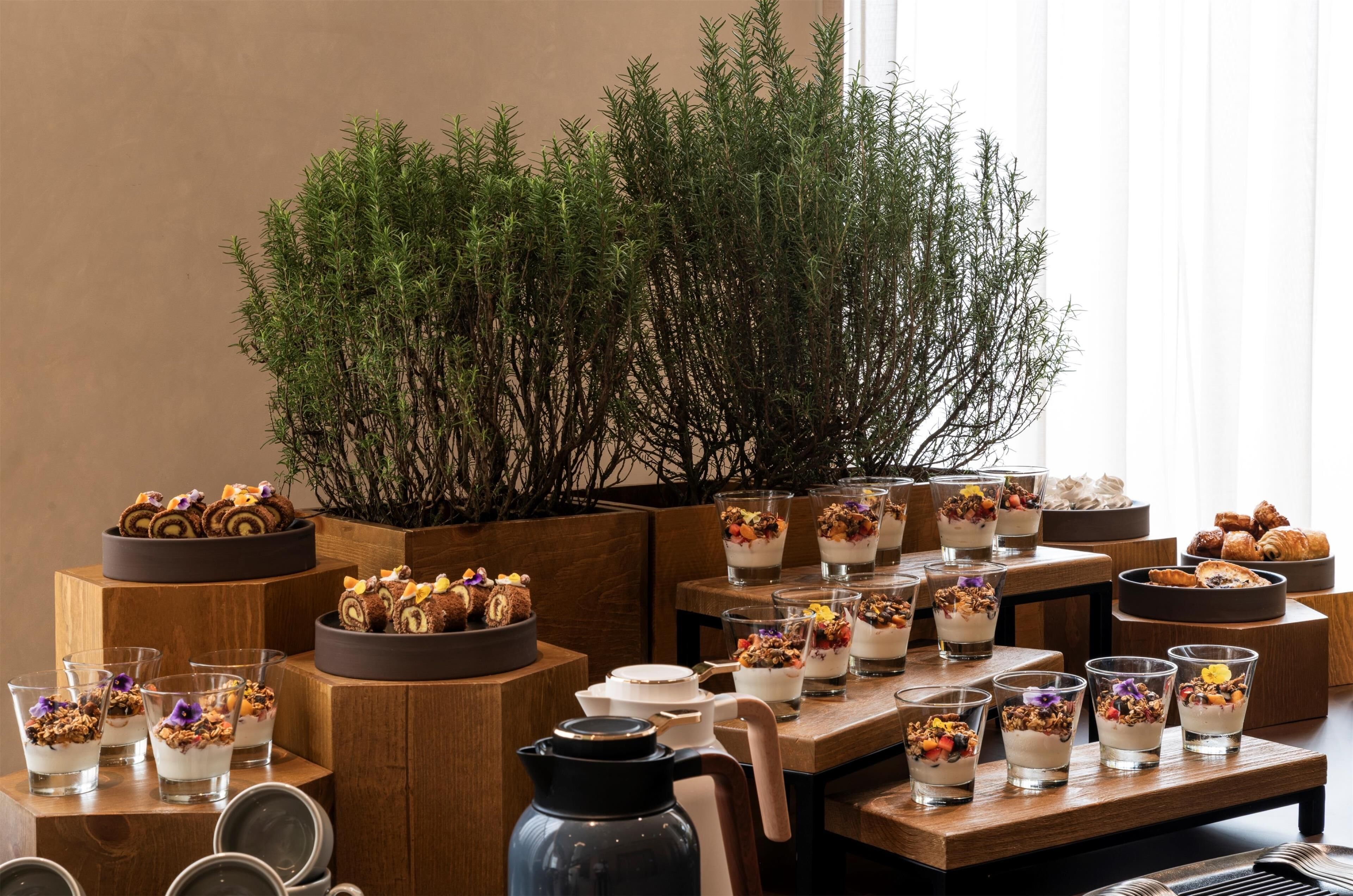A table with various desserts and drinks, surrounded by wooden furniture and a large plant.