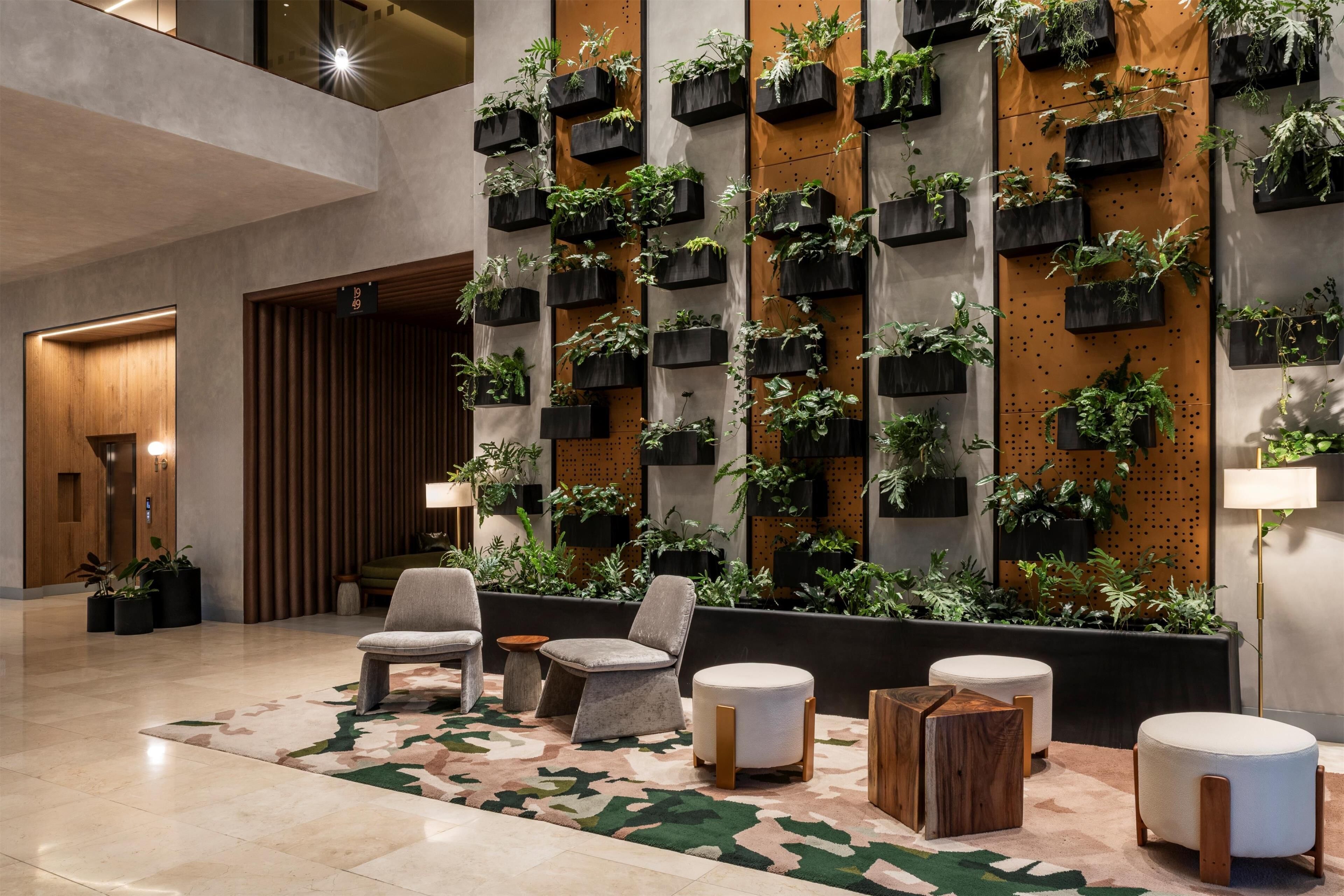 A lobby with a modern design, featuring a wall-mounted planter with various plants, comfortable seating, and a patterned carpet.