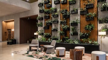 A lobby with a modern design, featuring a wall-mounted planter with various plants, comfortable seating, and a patterned carpet.