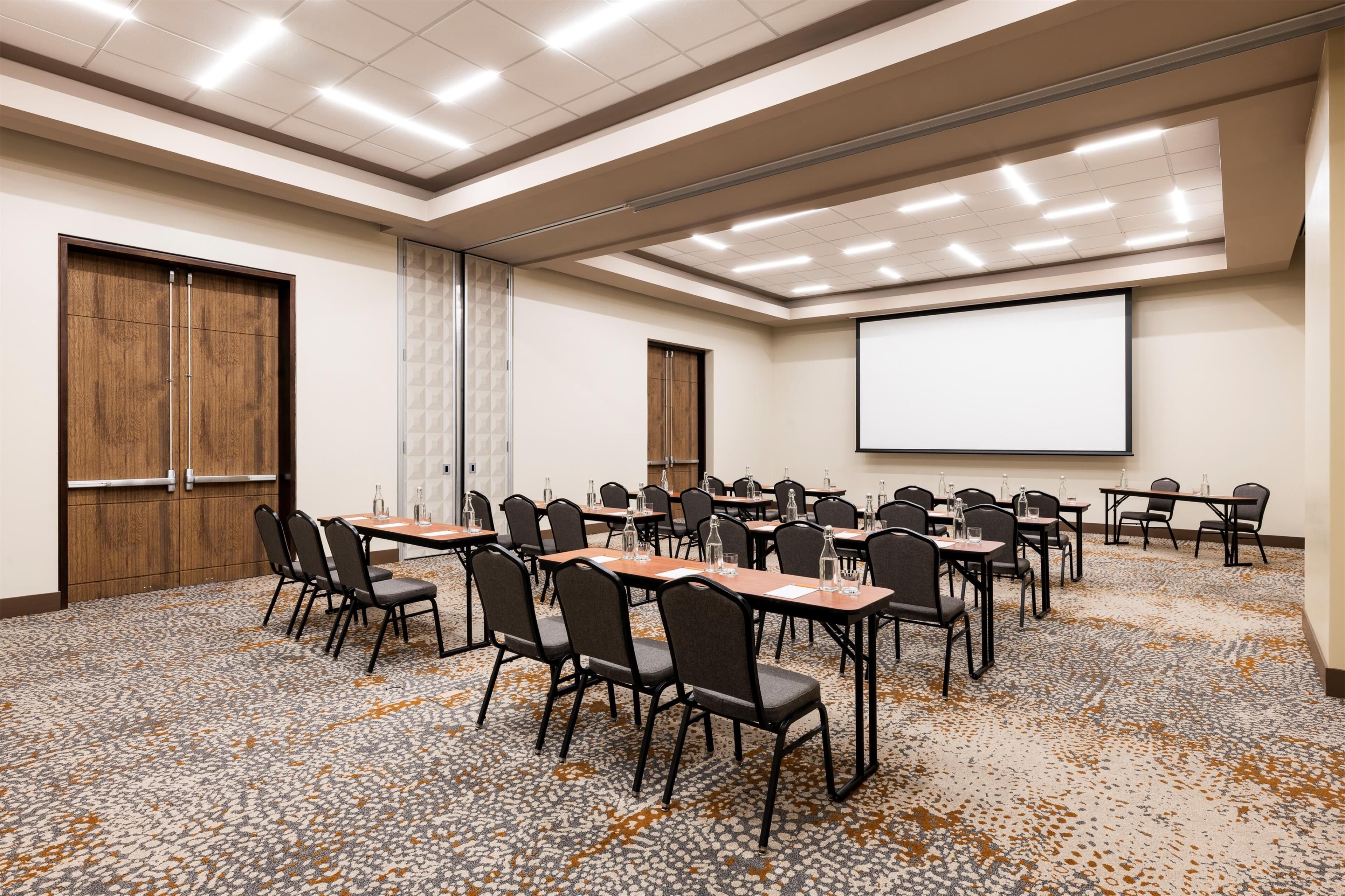Une salle de conférence équipée d’un grand écran, de plusieurs tables et de chaises disposées pour les réunions.