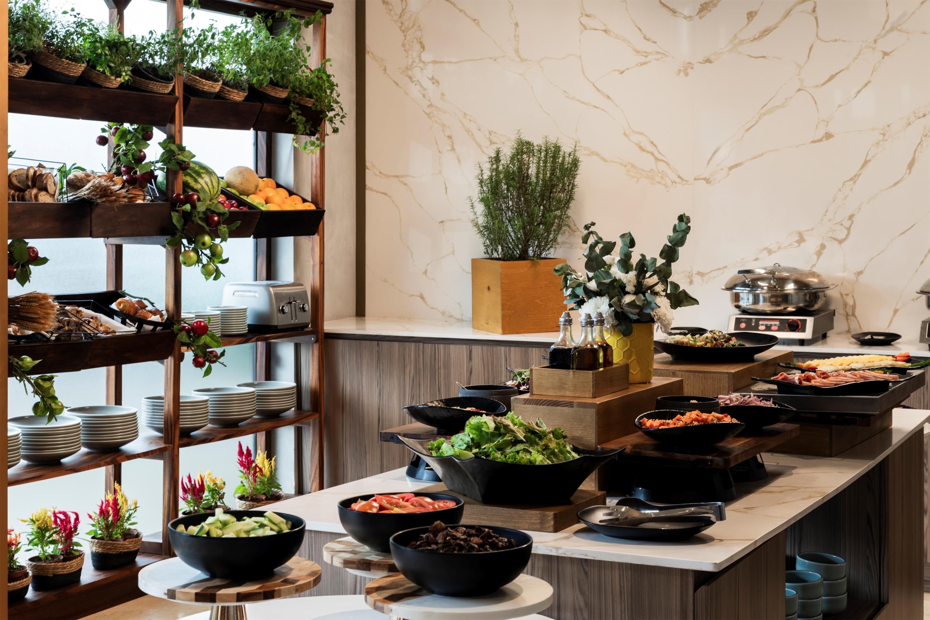 A buffet setup with various food items and a wooden shelf with fruits and vegetables.