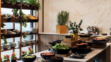 A buffet setup with various food items and a wooden shelf with fruits and vegetables.