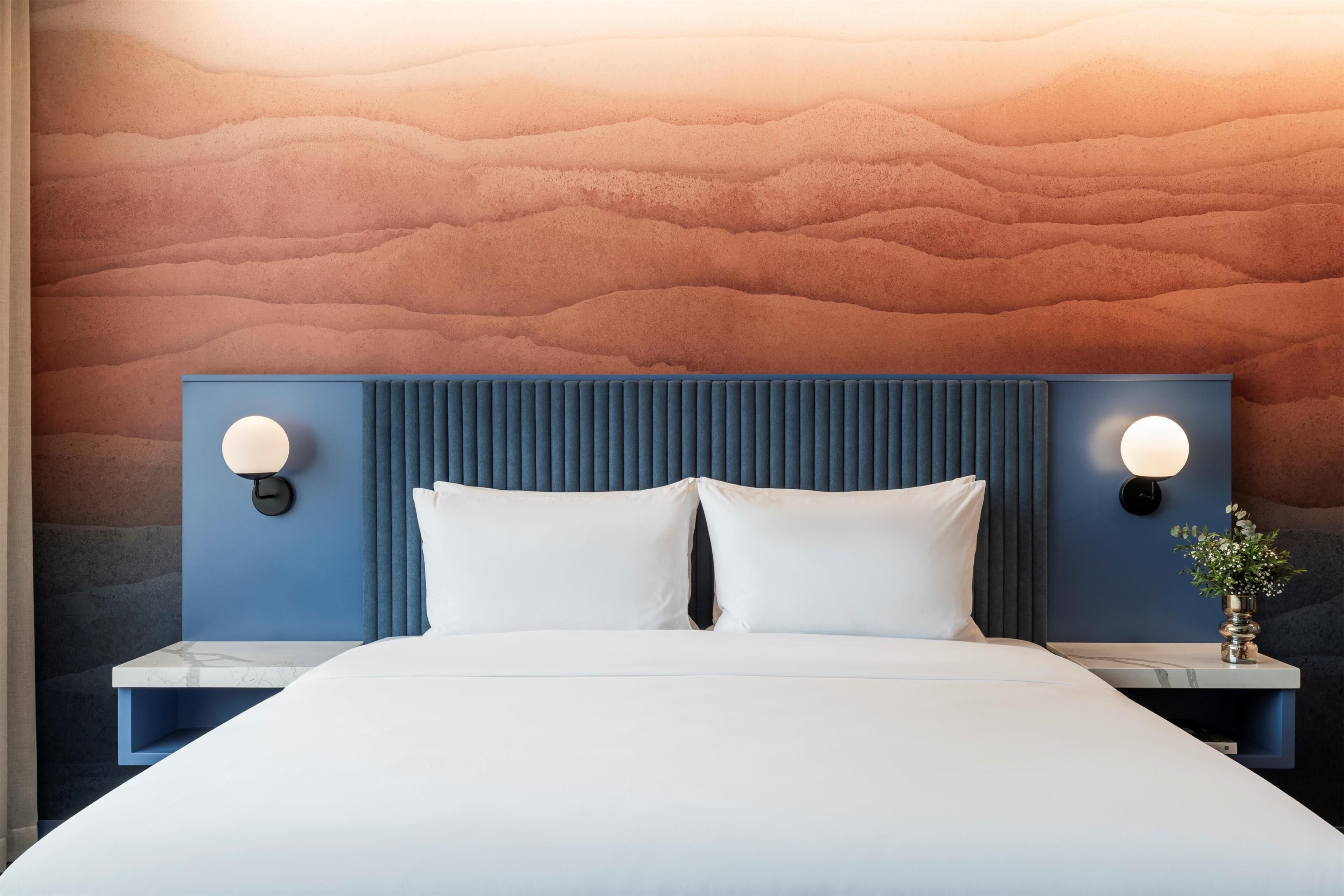 A modern hotel room with a large bed, two bedside tables, and a textured wall.