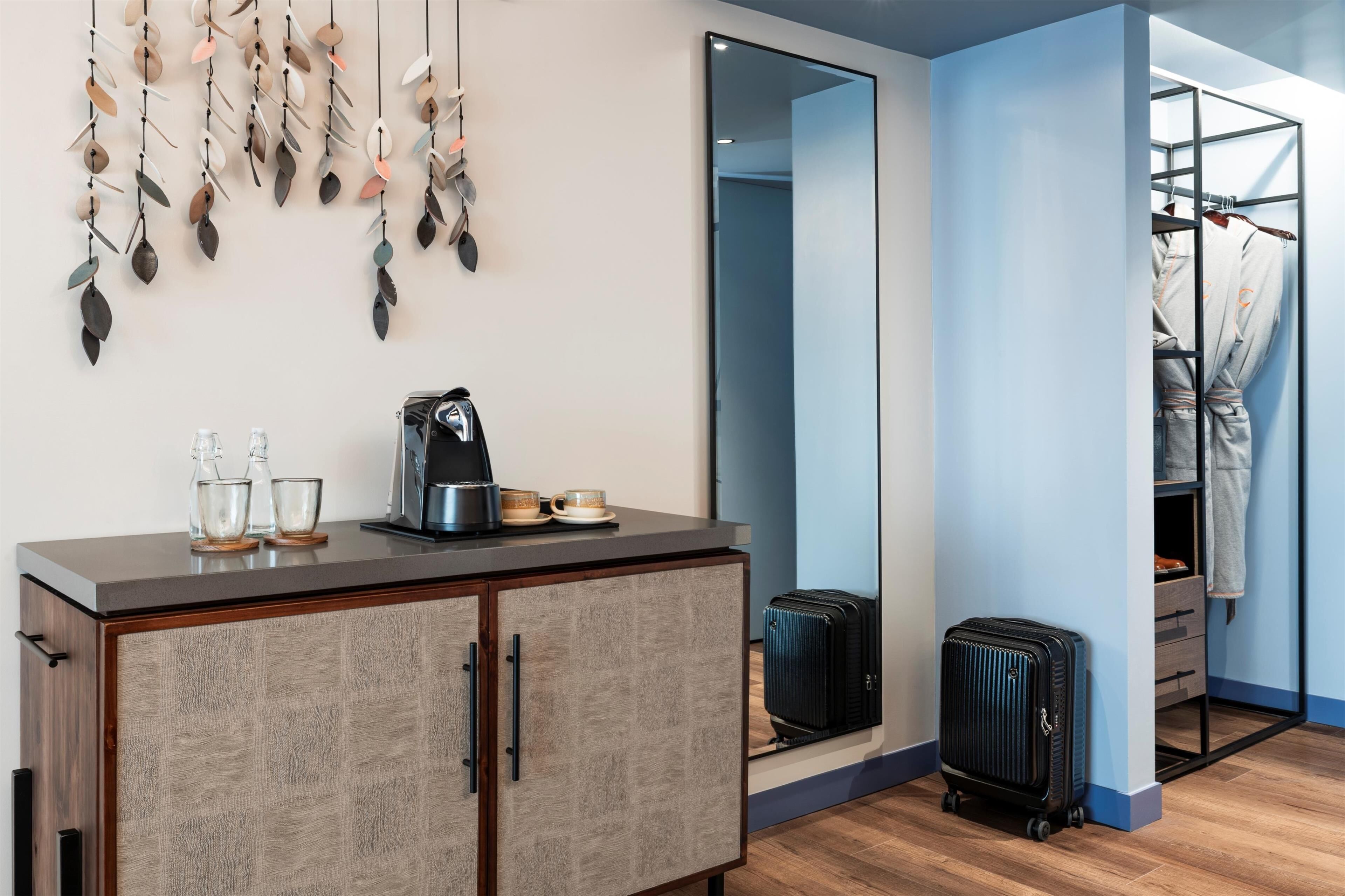 A hotel room with a wooden cabinet, a mirror, a suitcase, and a clothing rack.