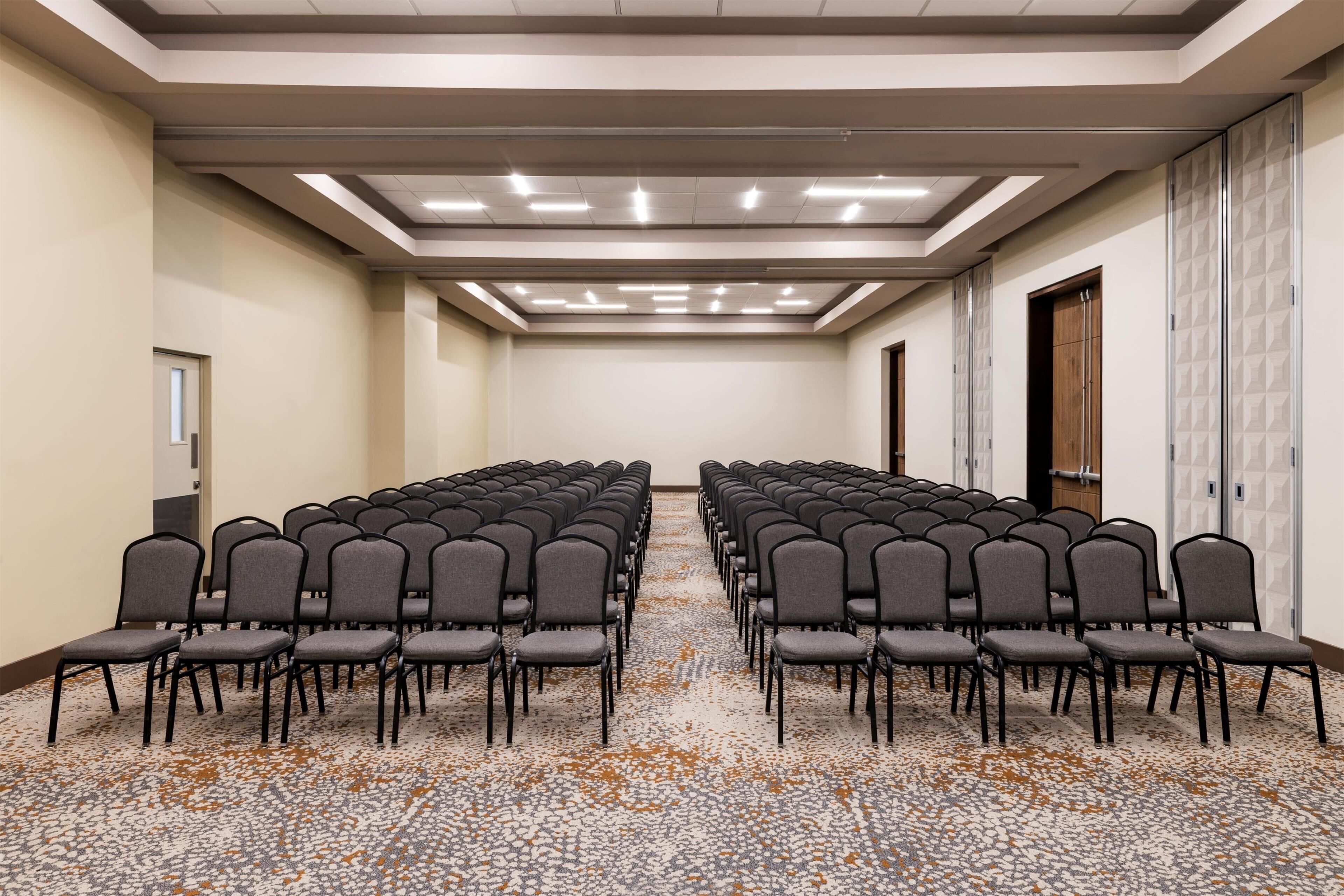Un salón de conferencias con filas de sillas, una alfombra estampada e iluminación empotrada en el techo.