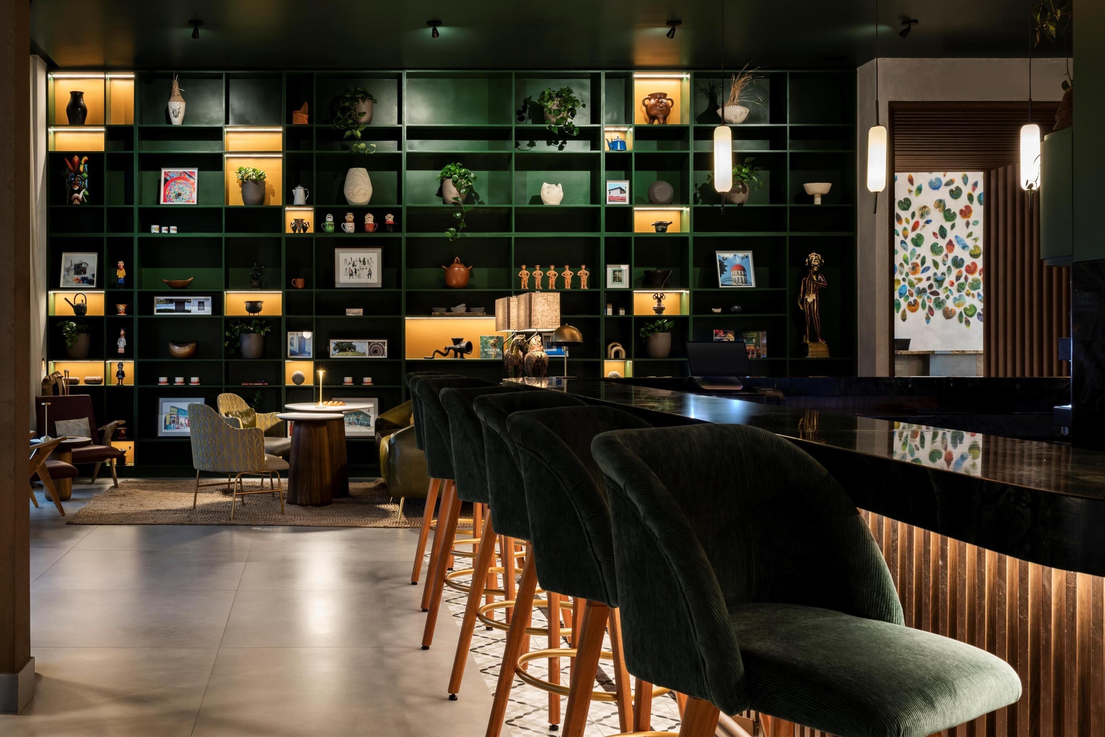 Un espace bar moderne avec des étagères vert foncé, des tabourets de bar et un éclairage d’ambiance.
