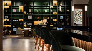 Un espace bar moderne avec des étagères vert foncé, des tabourets de bar et un éclairage d’ambiance.
