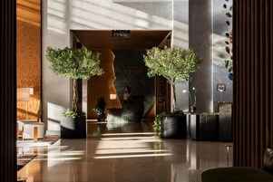 Un moderno vestíbulo de hotel con mostrador de recepción, plantas en macetas y una pared grande con diseño de grieta.