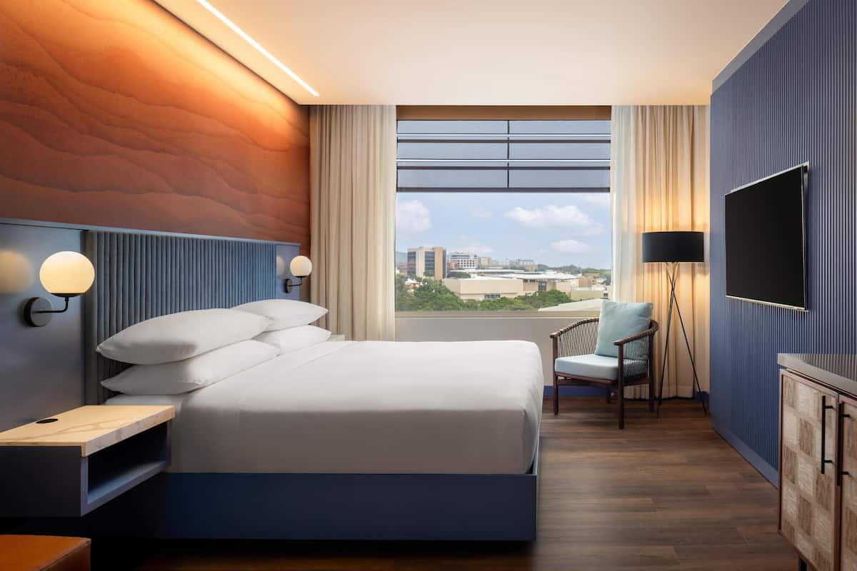 Une chambre d’hôtel moderne dotée d’un grand lit, d’une télévision, d’un bureau et offrant une vue sur la ville.