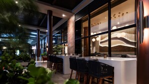 Un área de bar al aire libre con diseño moderno, que incluye una barra larga con taburetes y una lámpara decorativa colgante.