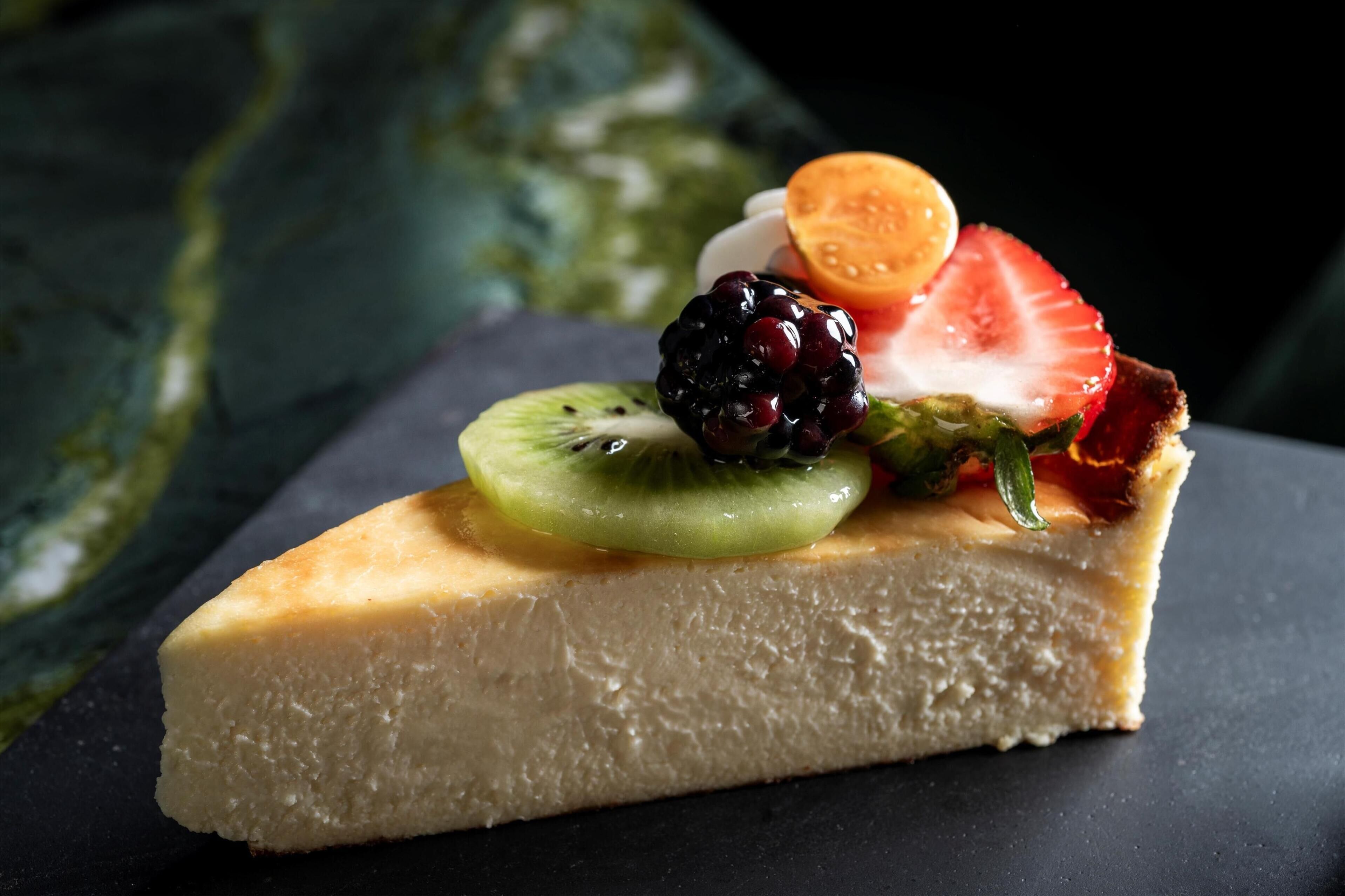 Ein Stück Käsekuchen mit Kiwi, Erdbeere, Brombeere und Orangenscheibe.