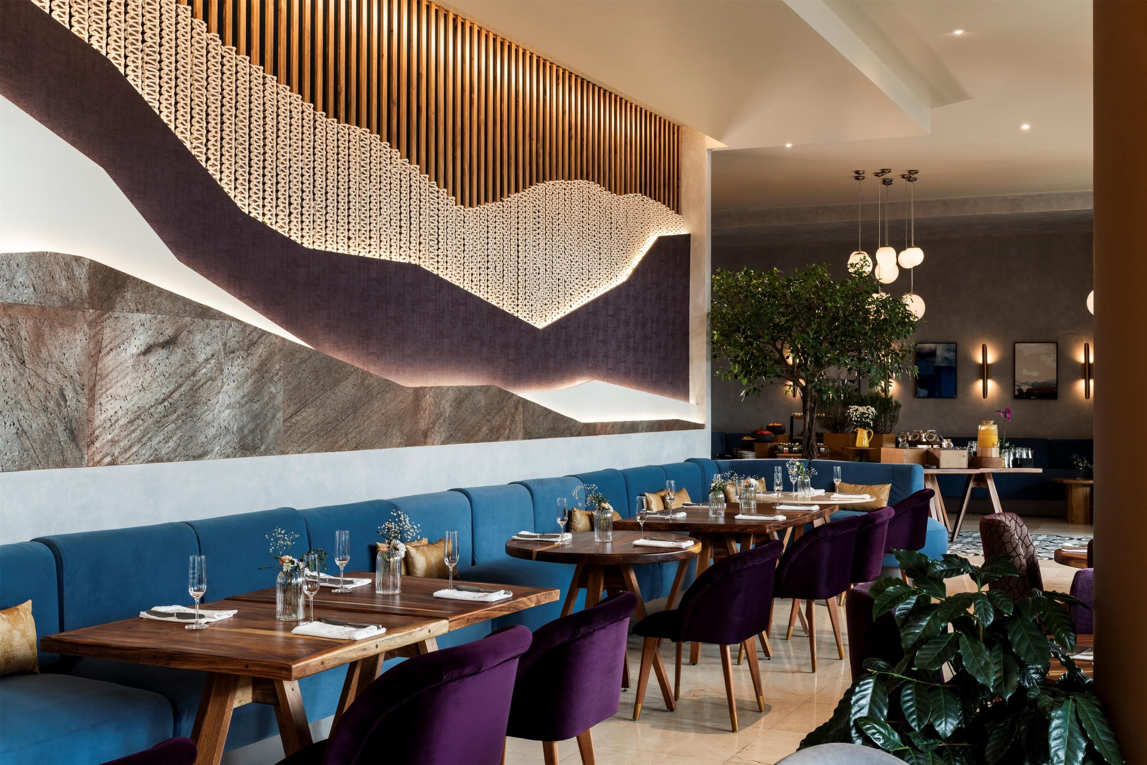 A modern restaurant with blue seating, wooden tables, and hanging pendant lights.