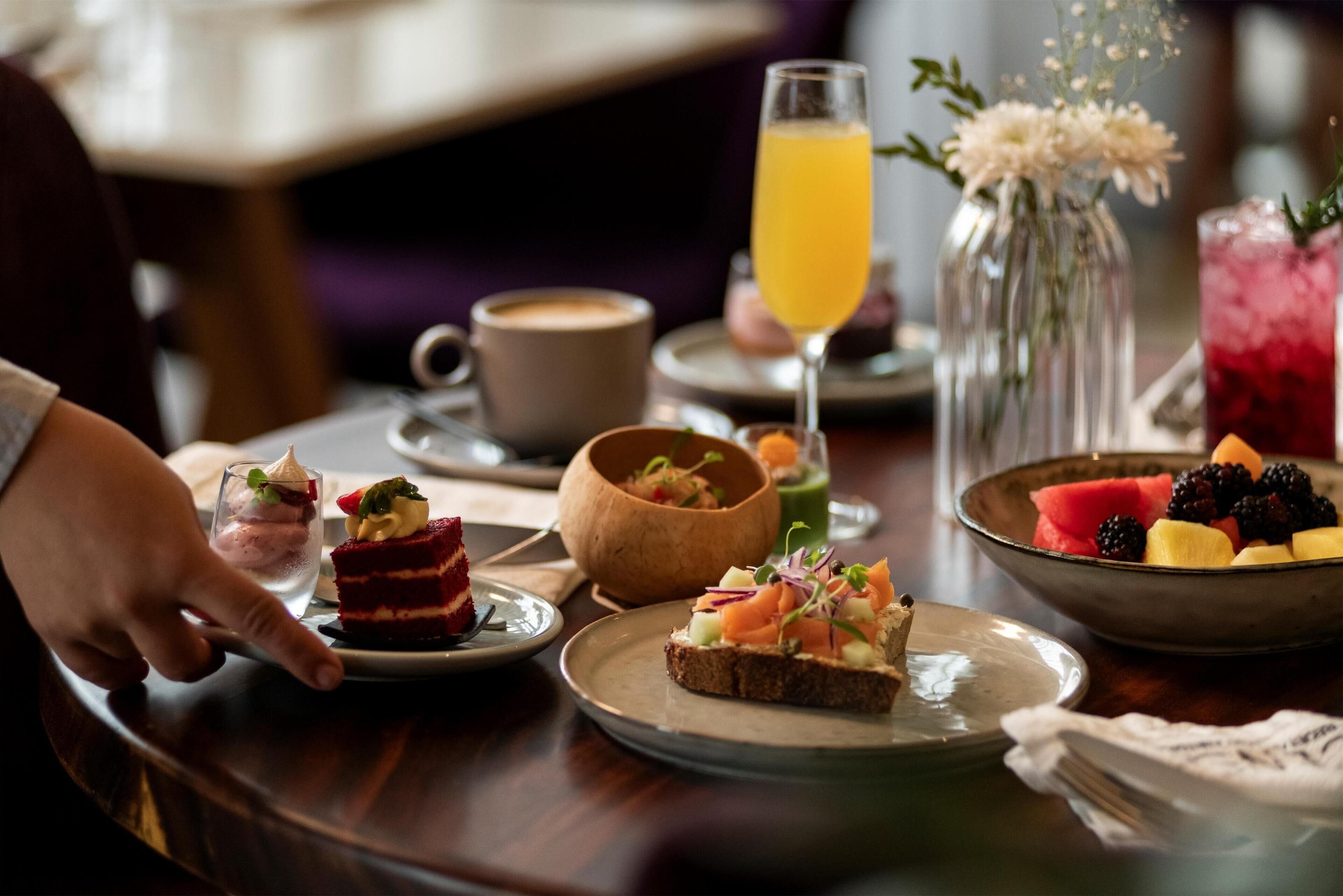 A dining table with various food items, including a slice of cake, a bowl of fruit, and a glass of orange juice.