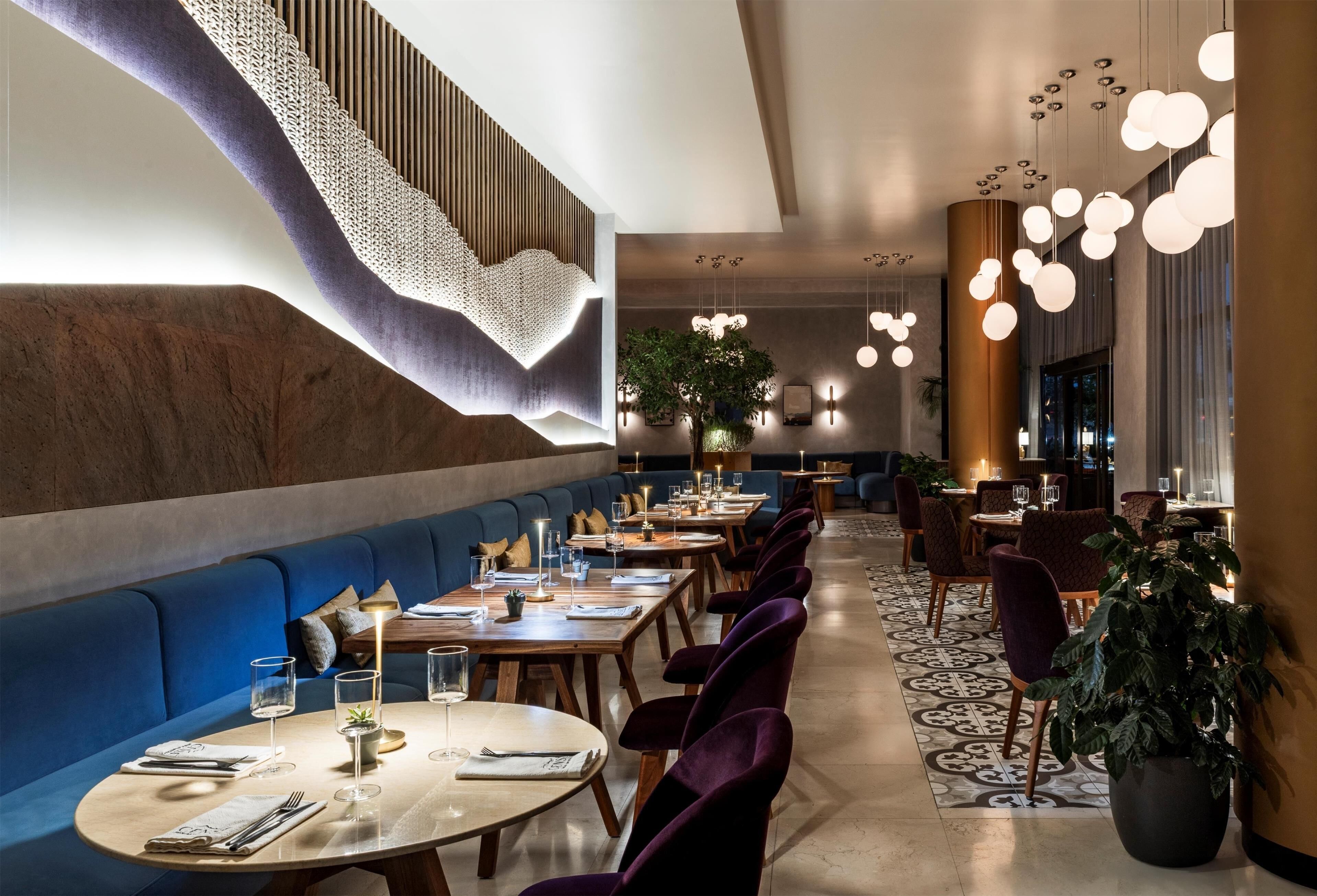 A restaurant with round tables, blue cushioned seating, and hanging spherical lights.
