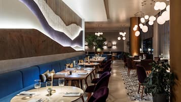 A restaurant with round tables, blue cushioned seating, and hanging spherical lights.