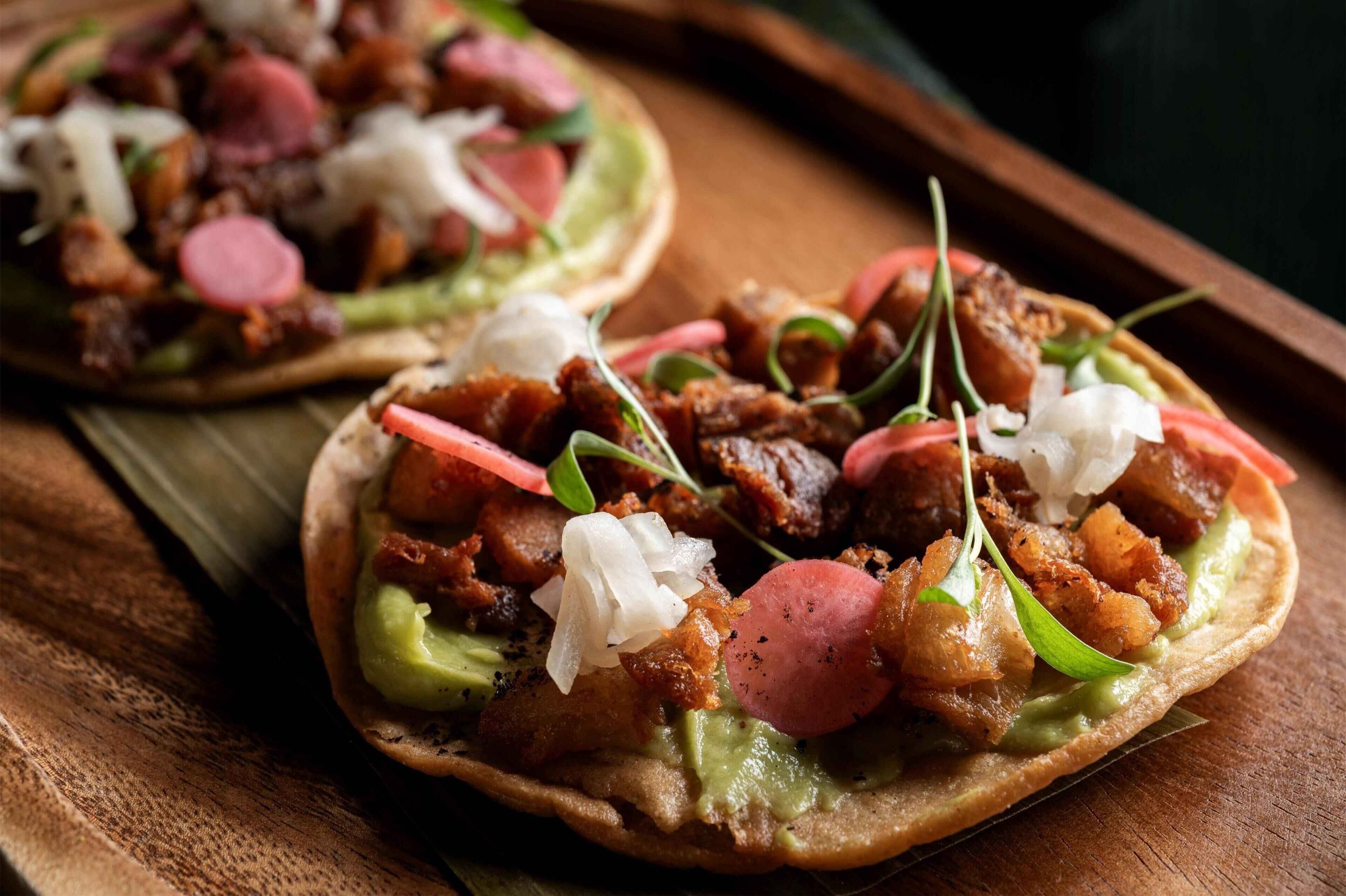 Two tacos with various toppings on a wooden surface.