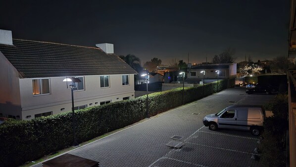 A residential street at night with houses, a parked car, and street lamps.