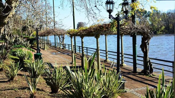 Un paseo marítimo de madera con faroles y plantas a lo largo de una senda junto al lago.