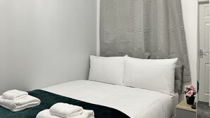 A neatly made bed with white linens, a dark green throw blanket, and two folded white towels on the bed. - Granada Apartments Holmfield Rd flat 3 1st floor front (Blackpool)