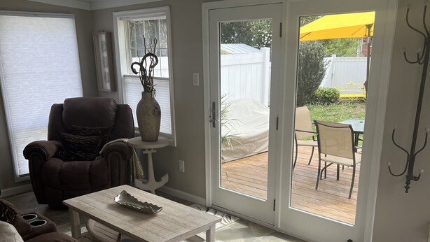 Une terrasse ensoleillée avec une porte-fenêtre coulissante, un fauteuil rembourré, une table basse et une table à manger.