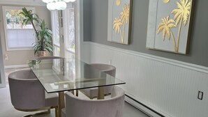 Un coin repas avec une table à plateau en verre, des chaises rembourrées et un luminaire suspendu.