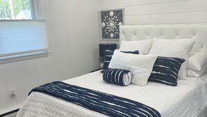 Une chambre à coucher moderne avec un grand lit, des murs blancs, une fenêtre avec des stores et un élément décoratif mural.