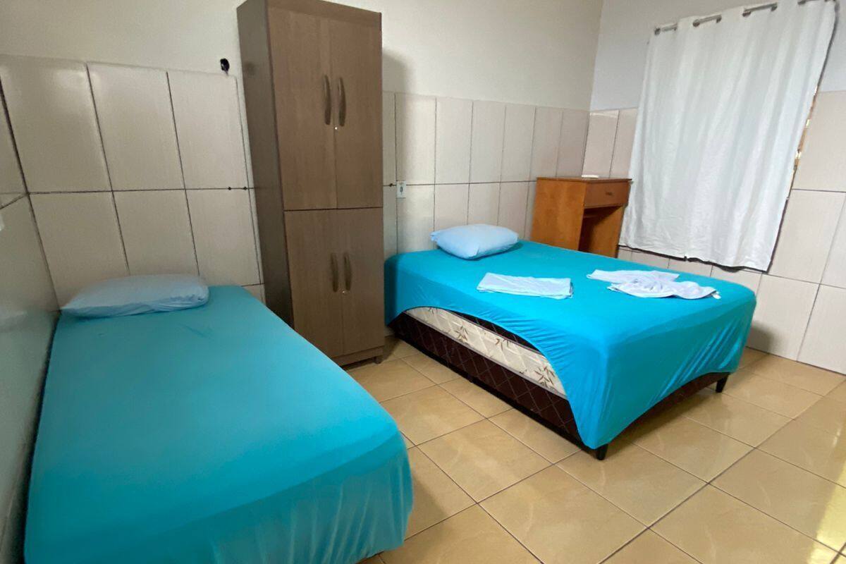 A room with two beds, a wardrobe, and a window with curtains.