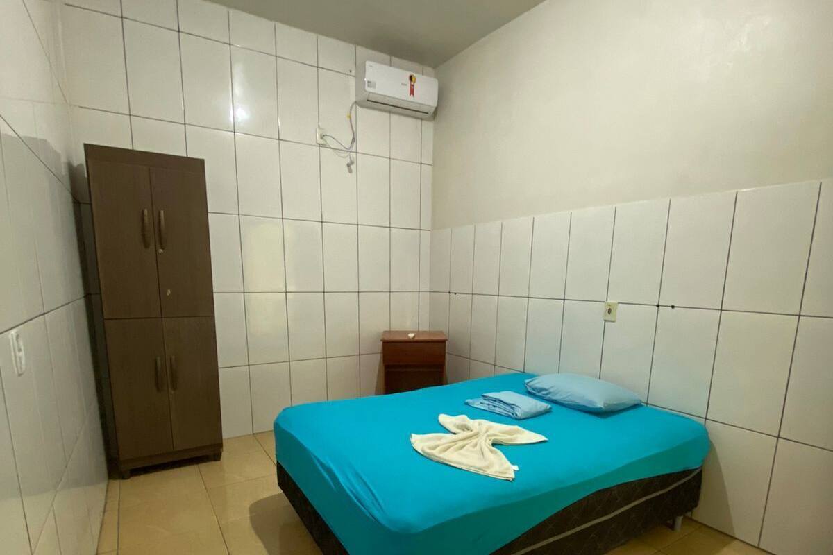 A small, clean room with a bed, a wardrobe, and an air conditioning unit on the wall.