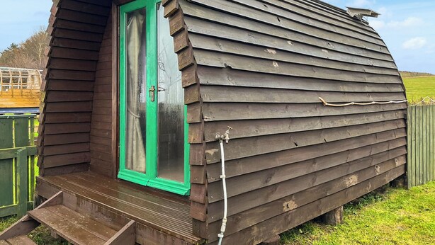 A wooden cabin with a green door, a small porch, and a sloped roof.