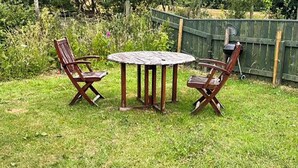 A wooden table and four chairs in a grassy outdoor area.
