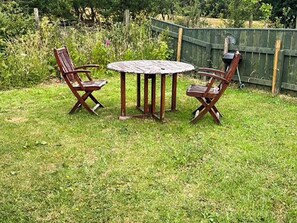 A wooden table and four chairs in a grassy outdoor area.